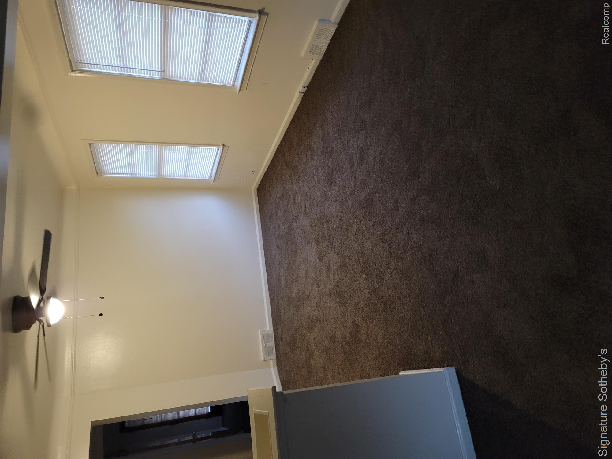 15241 Forrer Street Detroit, MI 48227 - Photo 8 of 10 Neutral tone wall paint, dark tone carpeting, two windows with blinds, and a ceiling fan with integrated lighting