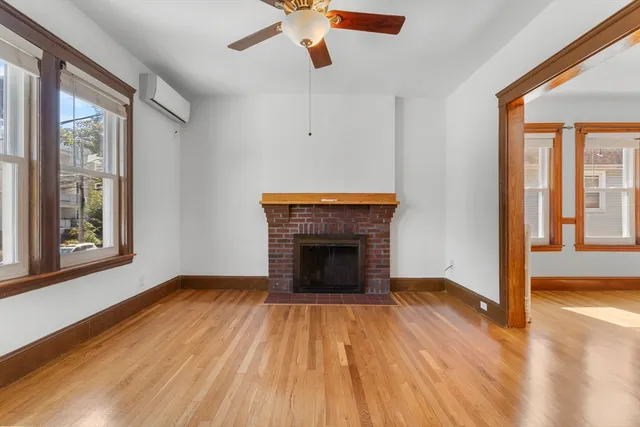 a view of an empty room with wooden floor fireplace and a window