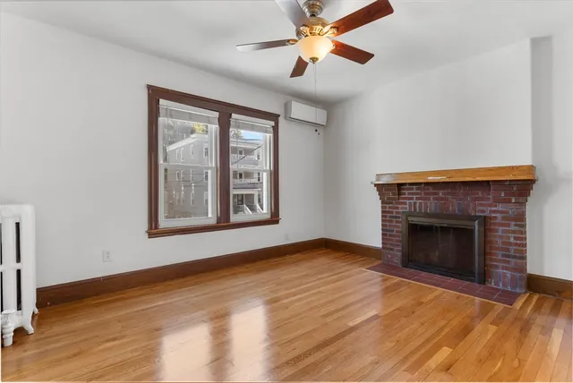 a view of an empty room with wooden floor fireplace and a window