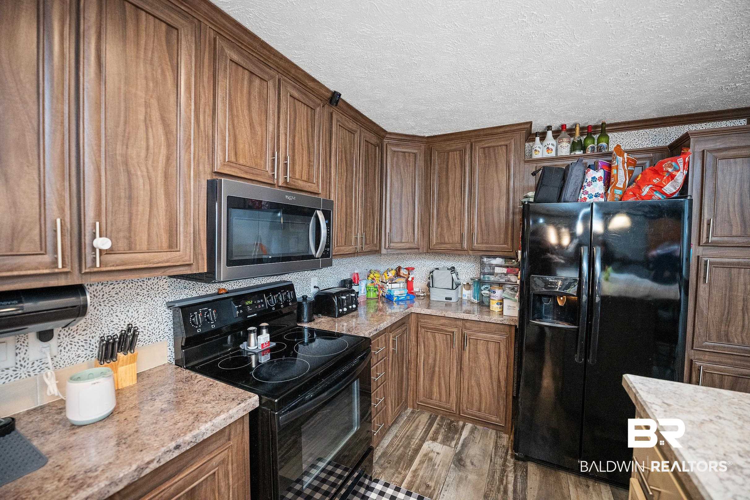 8630 Allison Lane Wilmer, AL 36587 - Photo 12 of 31 Kitchen featuring black appliances, a textured ceiling, decorative backsplash, brown cabinets, and dark wood-type flooring