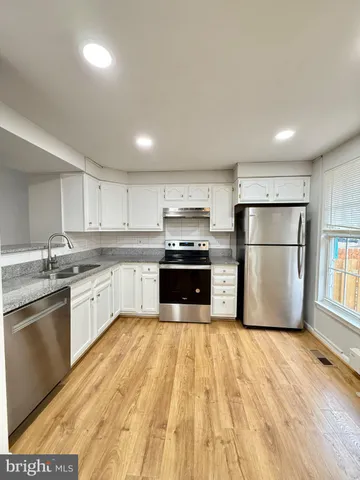 a large kitchen with granite countertop a refrigerator oven a sink dishwasher a stove and white cabinets with wooden floor