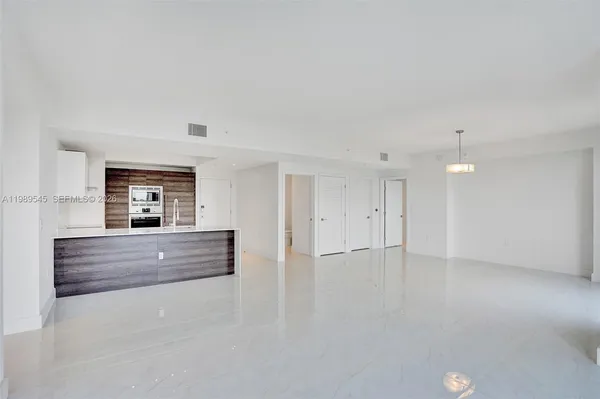 a view of an empty room with window and a kitchen