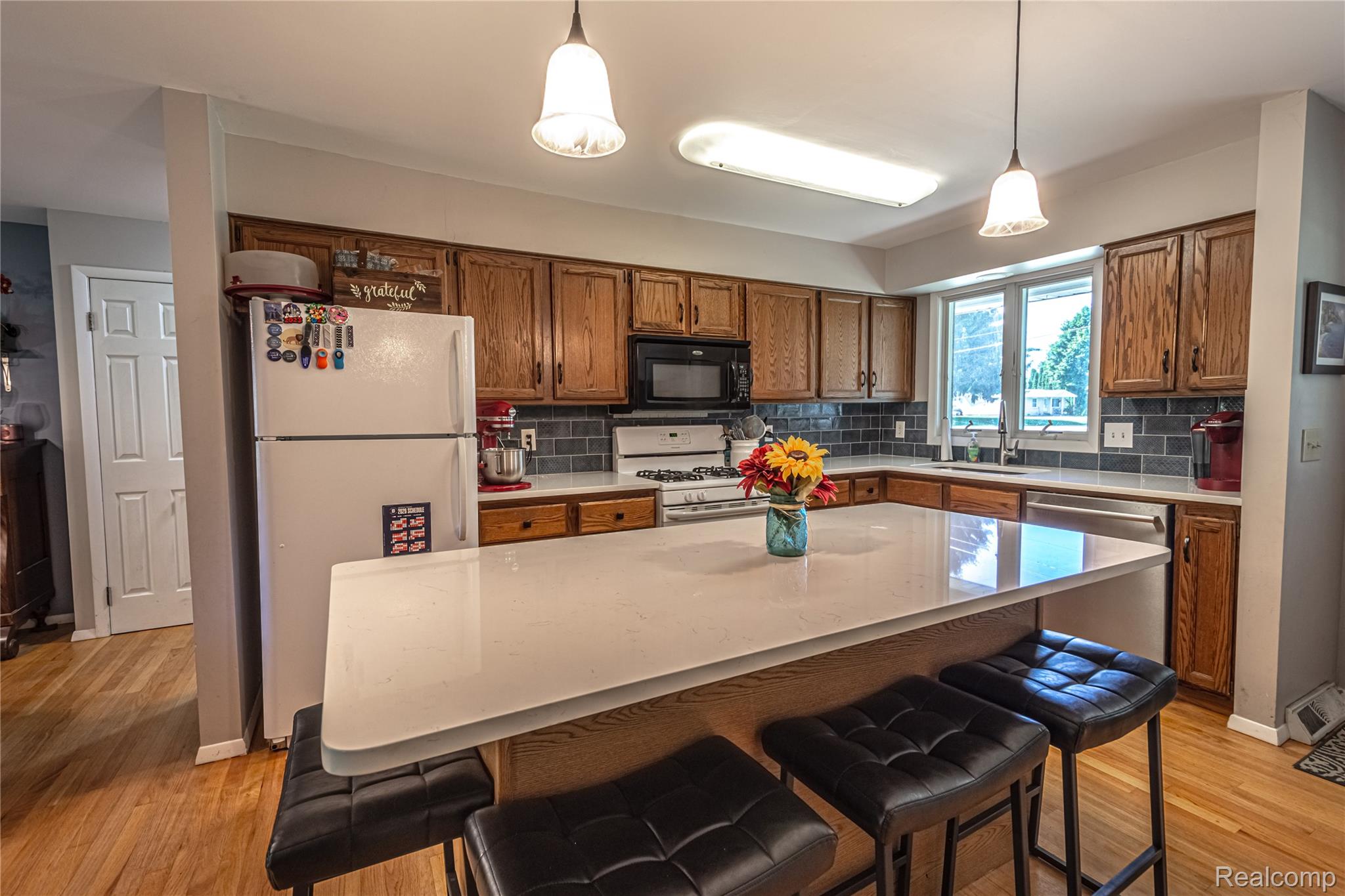 3241 Simpson Road Fort Gratiot, MI 48059 - Photo 12 of 27 Kitchen featuring a central island with countertop seating, wood-finish flooring, oak cabinetry, subway tile backsplash, and a large window above the sink
