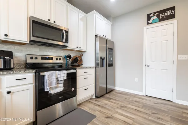 a kitchen with stainless steel appliances granite countertop a refrigerator stove and white cabinets with wooden floor