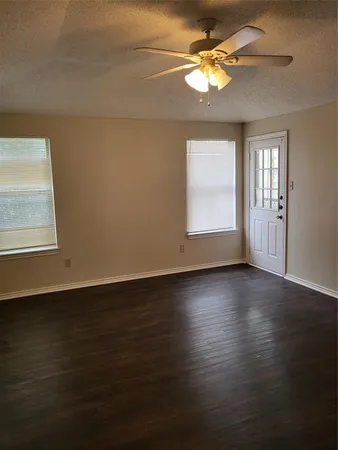 an empty room with wooden floor chandelier fan and windows