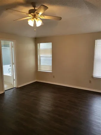 an empty room with wooden floor fan and windows