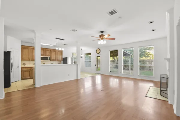 a view of an empty room with wooden floor and a kitchen