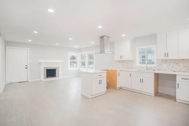 a large white kitchen with granite countertop a white stove a sink and dishwasher with white cabinets