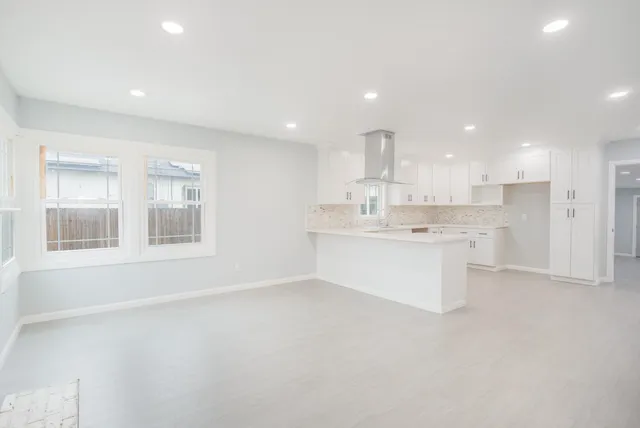 a large white kitchen with kitchen island a sink wooden floor and a refrigerator