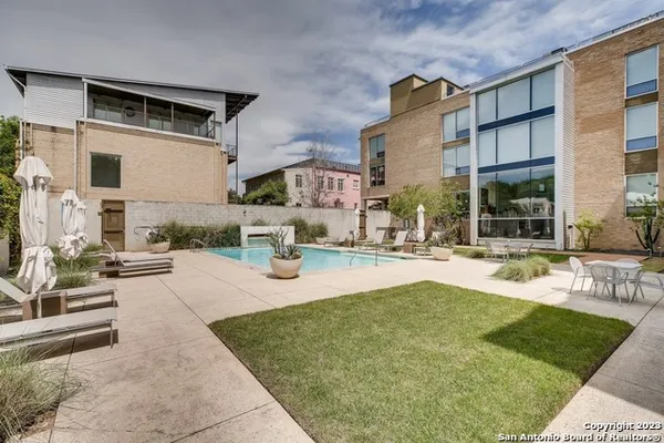a view of a swimming pool with lawn chairs plants and large tree