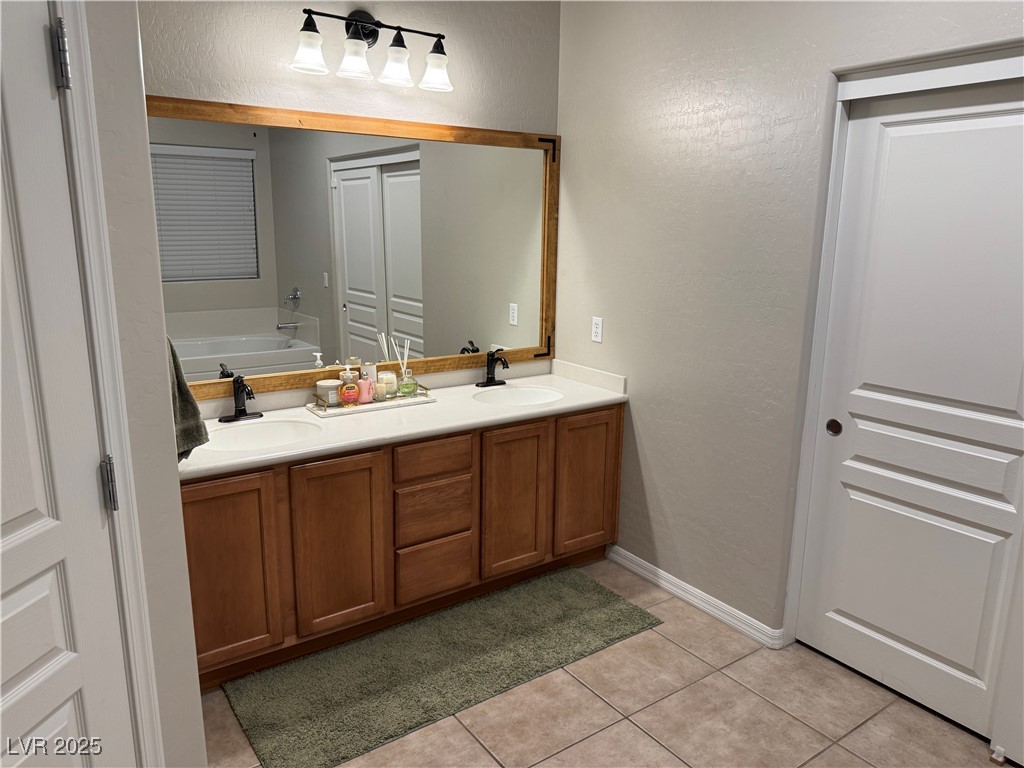5522 Porcupine Rim Street Las Vegas, NV 89130 - Photo 14 of 28 Bathroom with a textured wall, double vanity, a bath, light tile patterned flooring, and a closet