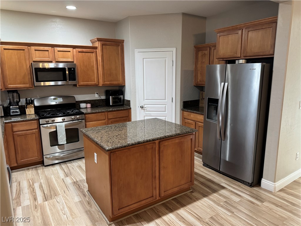 5522 Porcupine Rim Street Las Vegas, NV 89130 - Photo 3 of 28 Kitchen featuring stainless steel appliances, brown cabinetry, light wood-type flooring, dark stone countertops, and a kitchen island