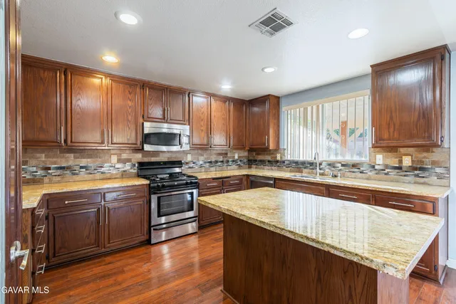 a kitchen with stainless steel appliances granite countertop wooden cabinets a stove top oven a sink and dishwasher with wooden floor