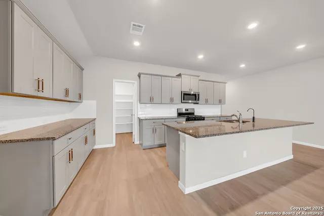 a kitchen with kitchen island granite countertop a sink a stove a microwave and cabinets