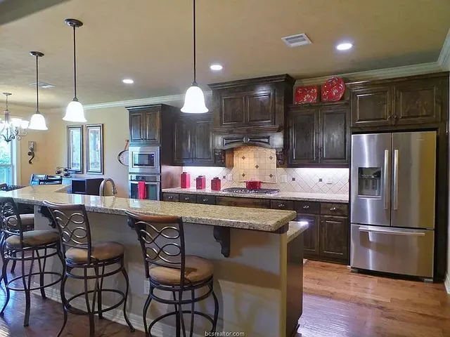 a kitchen with stainless steel appliances a dining table chairs refrigerator and microwave