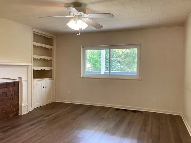 an empty room with wooden floor chandelier fan and windows