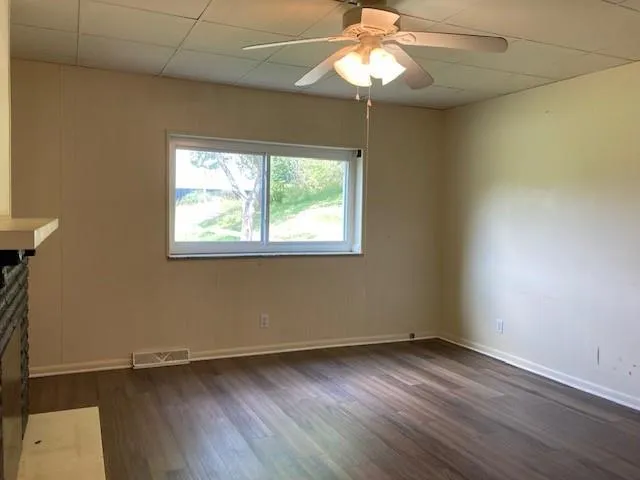 an empty room with wooden floor chandelier fan and windows