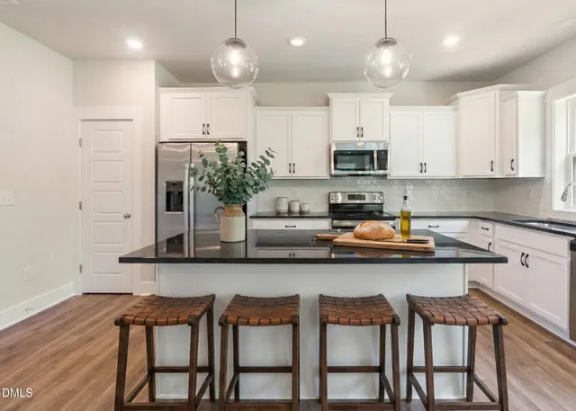 a kitchen with stainless steel appliances granite countertop a stove top oven a refrigerator a sink and white cabinets with wooden floor