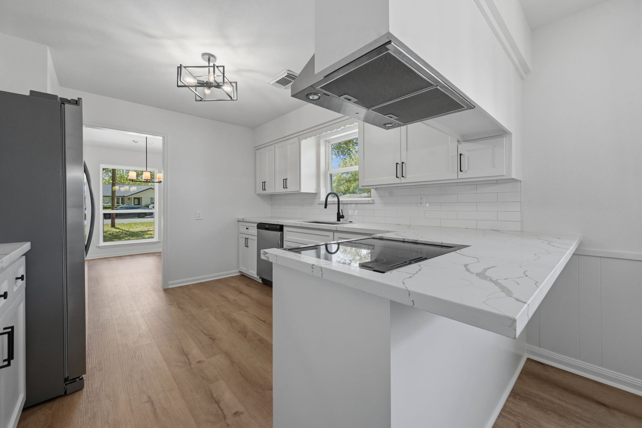 210 Ridgemont Drive Alvin, TX 77511 - Photo 7 of 27 Modern kitchen with white cabinetry and marble countertops. Features an island cooktop, stainless steel appliances, and wood flooring. Bright and open with a window overlooking the backyard.