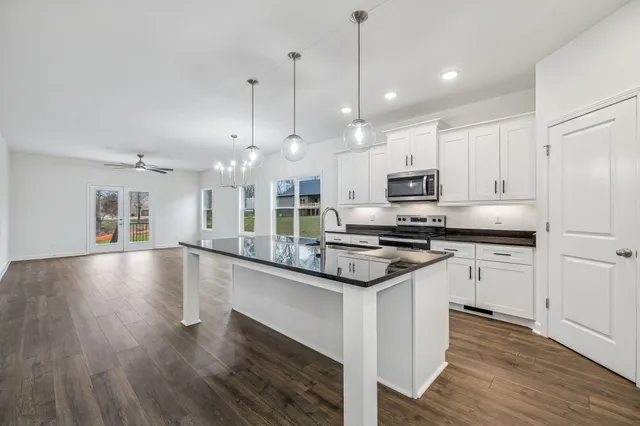 a kitchen with stainless steel appliances granite countertop a sink a stove a refrigerator and white cabinets with wooden floor