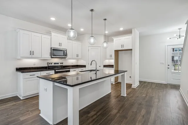 a kitchen with kitchen island granite countertop a sink a stove a oven a refrigerator cabinets and a wooden floor