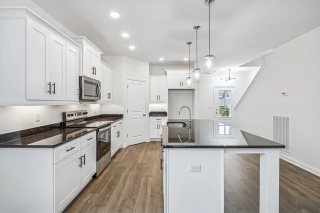 a large kitchen with stainless steel appliances granite countertop a stove a sink a refrigerator and white cabinets with wooden floor