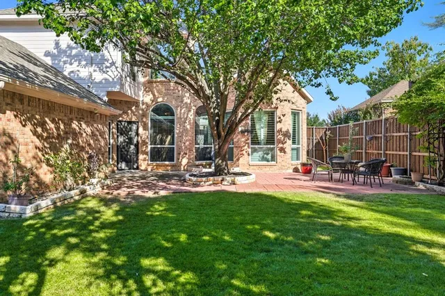 a view of a backyard with table and chairs potted plants and large tree