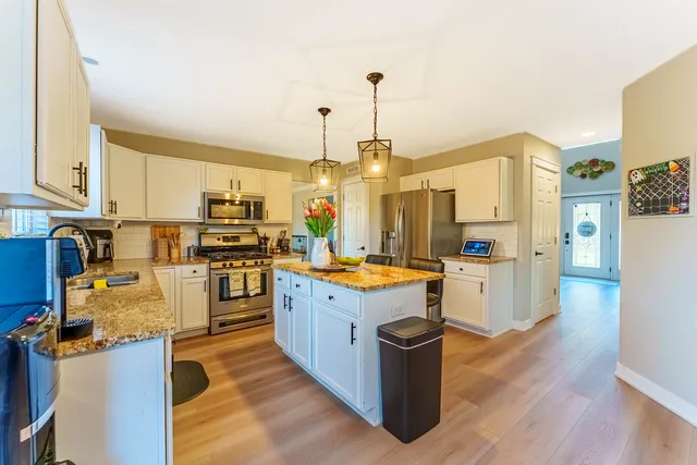a kitchen with stainless steel appliances kitchen island granite countertop a stove top oven a sink dishwasher and a refrigerator with wooden floor