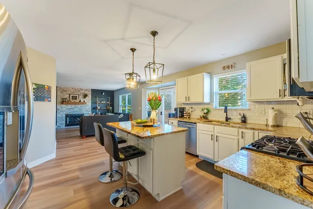 a kitchen with stainless steel appliances granite countertop a stove a sink dishwasher a refrigerator a dining table and chairs with wooden floor