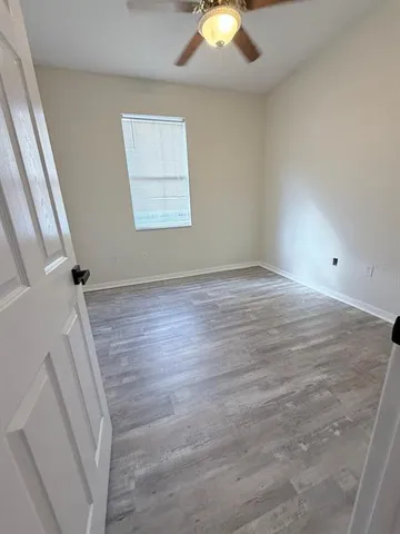 an empty room with wooden floor fan and windows