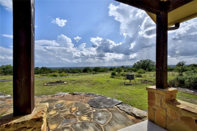 633 Trails End Road Johnson City, TX 78636 - Photo 5 of 29 A stone patio framed by rustic pillars looks out over a wide grassy landscape.