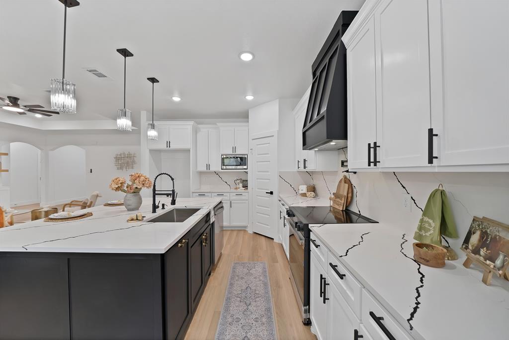 805 Tierney Road Fort Worth, TX 76112 - Photo 11 of 36 Kitchen featuring white cabinetry with black hardware, an expansive island with an undermount sink, light wood-finish flooring, and white countertops with dark veining