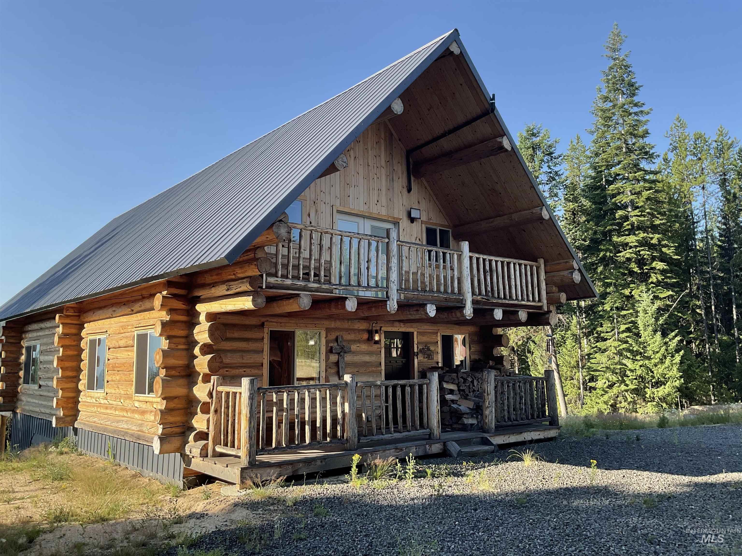 625 Rhett Creek Road Elk City, ID 83525 - Photo 8 of 48 Log home exterior featuring a metal roof, an upper-level balcony with log railing, and a ground-level covered porch with log detailing