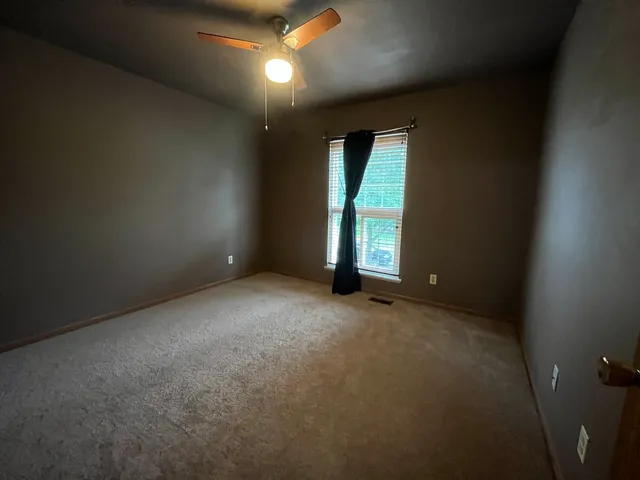 an empty room with a window and chandelier fan