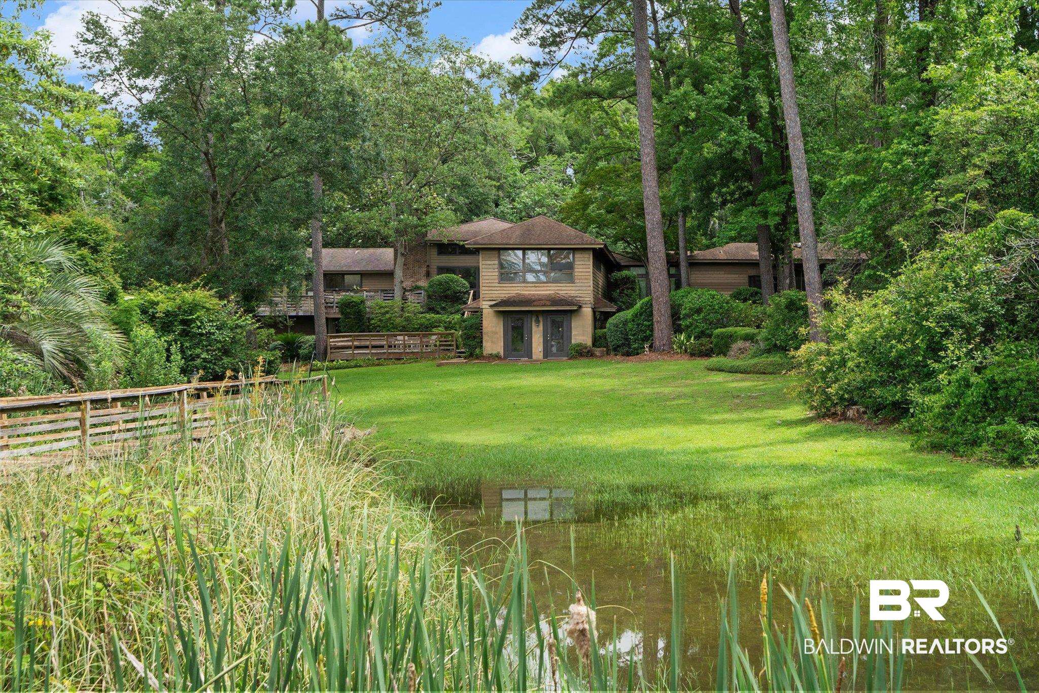 3500 Venetia Road Mobile, AL 36605 - Photo 52 of 56 Expansive waterfront property featuring a large green lawn, mature trees, a wooden boardwalk, and a multi-level residence with a tan facade and dark trim