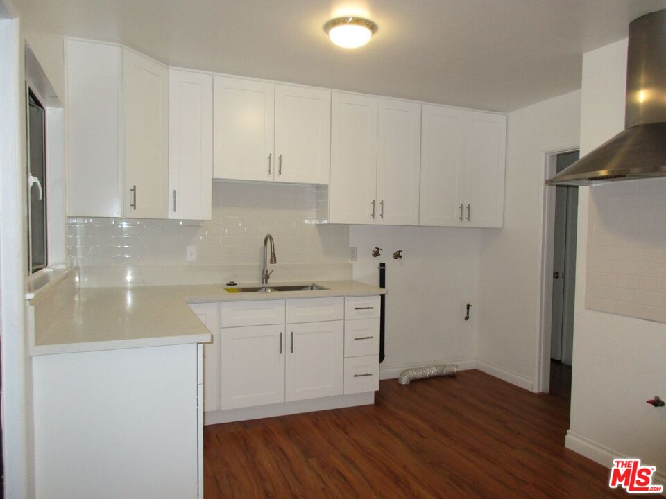 719 East 154th Street Compton, CA 90220 - Photo 11 of 32 a kitchen with wooden floors and white cabinets