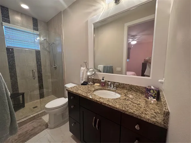 a bathroom with a granite countertop sink a toilet a mirror and shower