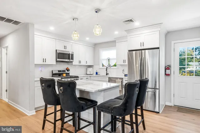 a kitchen with stainless steel appliances kitchen island granite countertop a sink dishwasher a stove a refrigerator oven a dining table and chairs with wooden floor