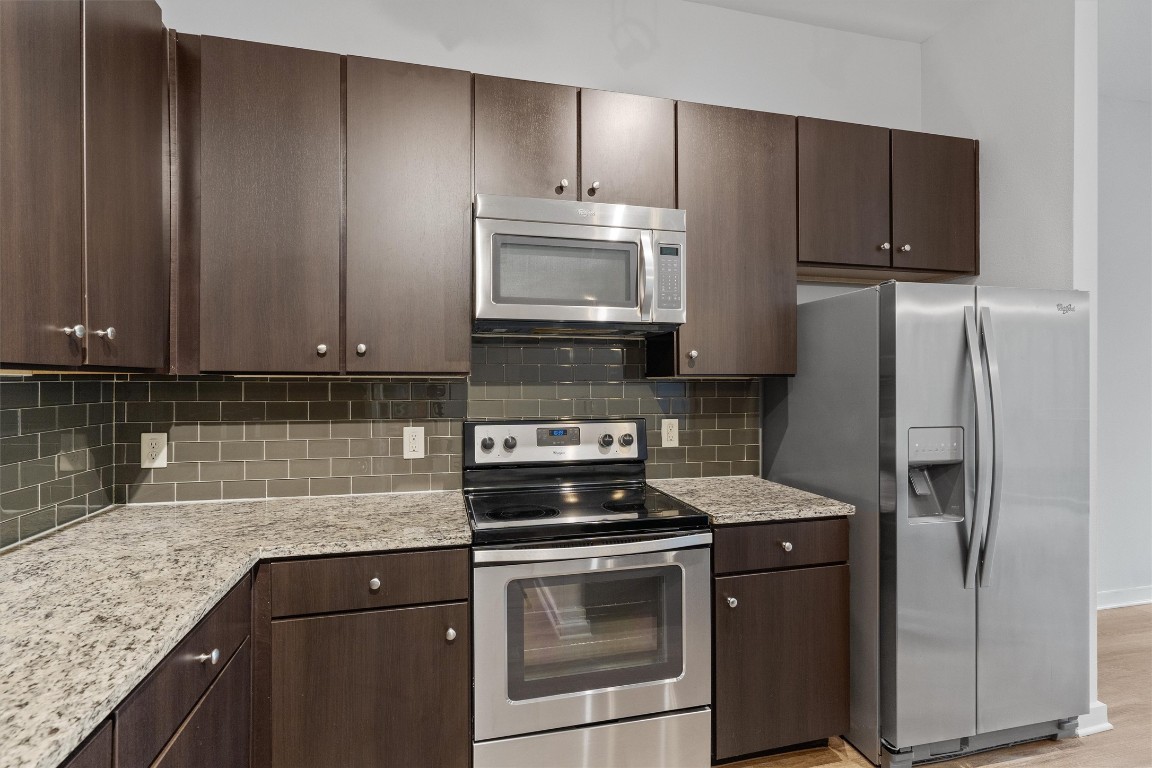 1900 Barton Springs Road, Unit 2027 Austin, TX 78704 - Photo 5 of 28 Kitchen featuring dark brown cabinetry, stainless steel appliances, light stone counters, light wood-style floors, and backsplash