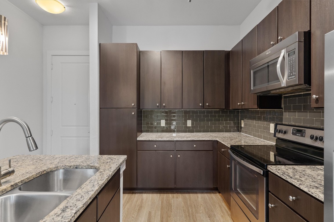 1900 Barton Springs Road, Unit 2027 Austin, TX 78704 - Photo 6 of 28 Kitchen with stainless steel appliances, dark brown cabinets, light stone counters, and light wood-style floors