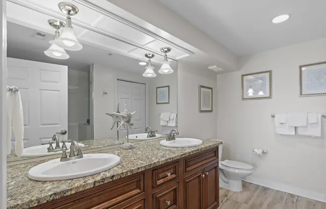 a bathroom with a granite countertop double vanity sink a toilet and a mirror
