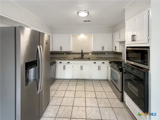 a kitchen with stainless steel appliances granite countertop a stove top oven a sink a refrigerator and cabinets