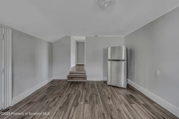 a view of empty room with wooden floor and kitchen