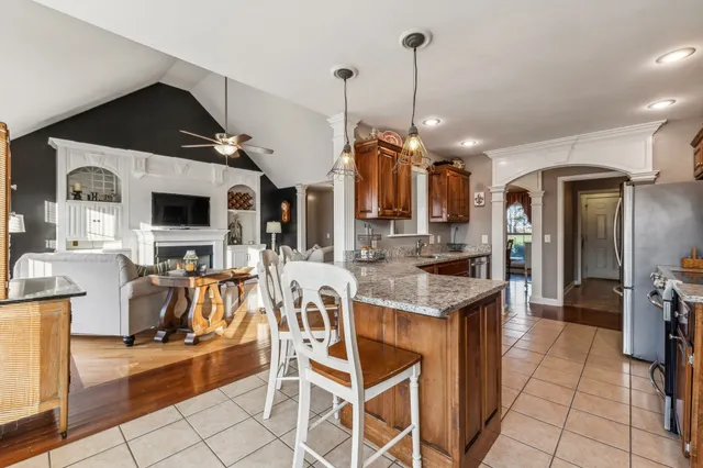 a kitchen with stainless steel appliances kitchen island granite countertop a refrigerator a stove a microwave oven a dining table and chairs with the view of living room