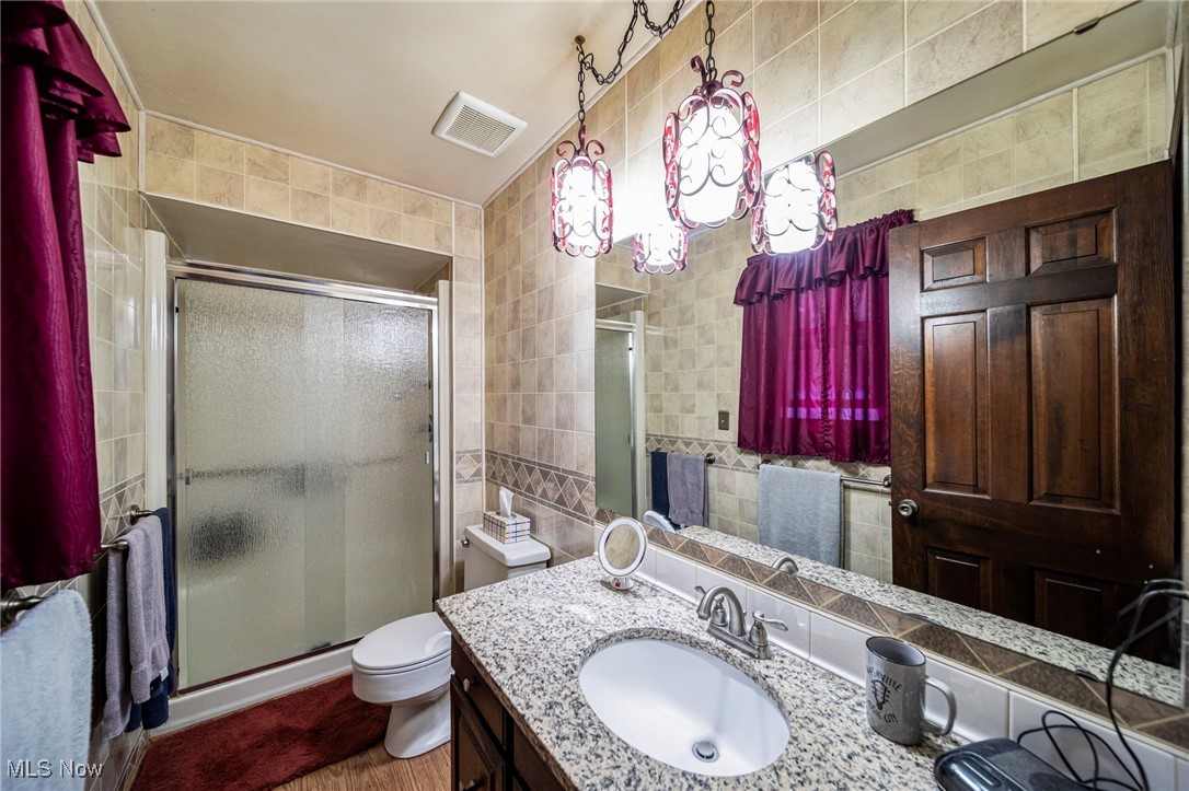 2921 Sexton Road Geneva, OH 44041 - Photo 43 of 43 Full bathroom featuring a shower stall, tile walls, vanity, dark wood finished floors, and decorative backsplash
