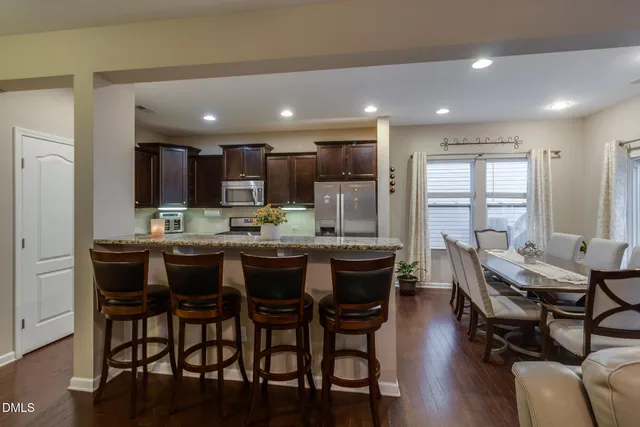 a dining area with stainless steel appliances kitchen island granite countertop a dining table chairs and a refrigerator