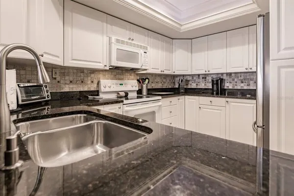 a kitchen with granite countertop a sink stainless steel appliances and white cabinets