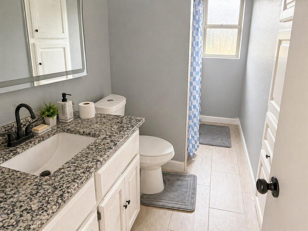 812 Irwin Drive Hurst, TX 76053 - Photo 10 of 16 Bathroom featuring a granite-finish countertop with an undermount sink, white vanity cabinetry, and a framed mirror