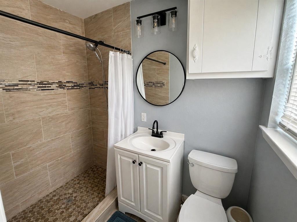812 Irwin Drive Hurst, TX 76053 - Photo 4 of 16 Bathroom featuring a walk-in shower with large format wall tiles and a mosaic floor, a single vanity with a white countertop and basin, a black finish faucet, and an overhead lighting fixture
