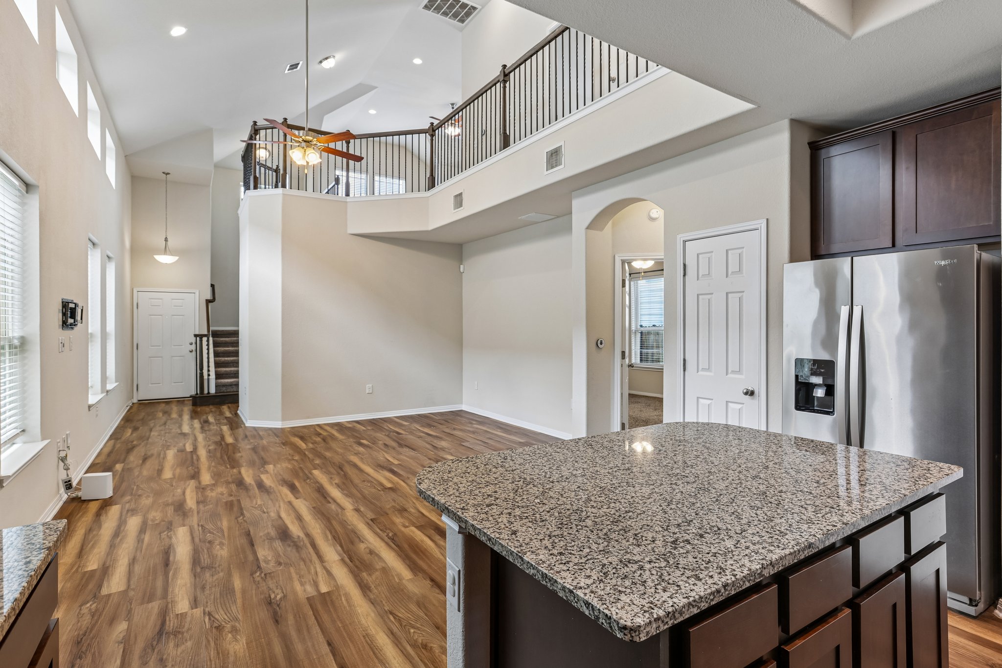 808 Totis Road Austin, TX 78748 - Photo 12 of 40 Open-concept living space featuring wood-finish flooring, a two-story ceiling, a second-story balcony with metal railing, an island with a speckled countertop, and dark wood cabinetry